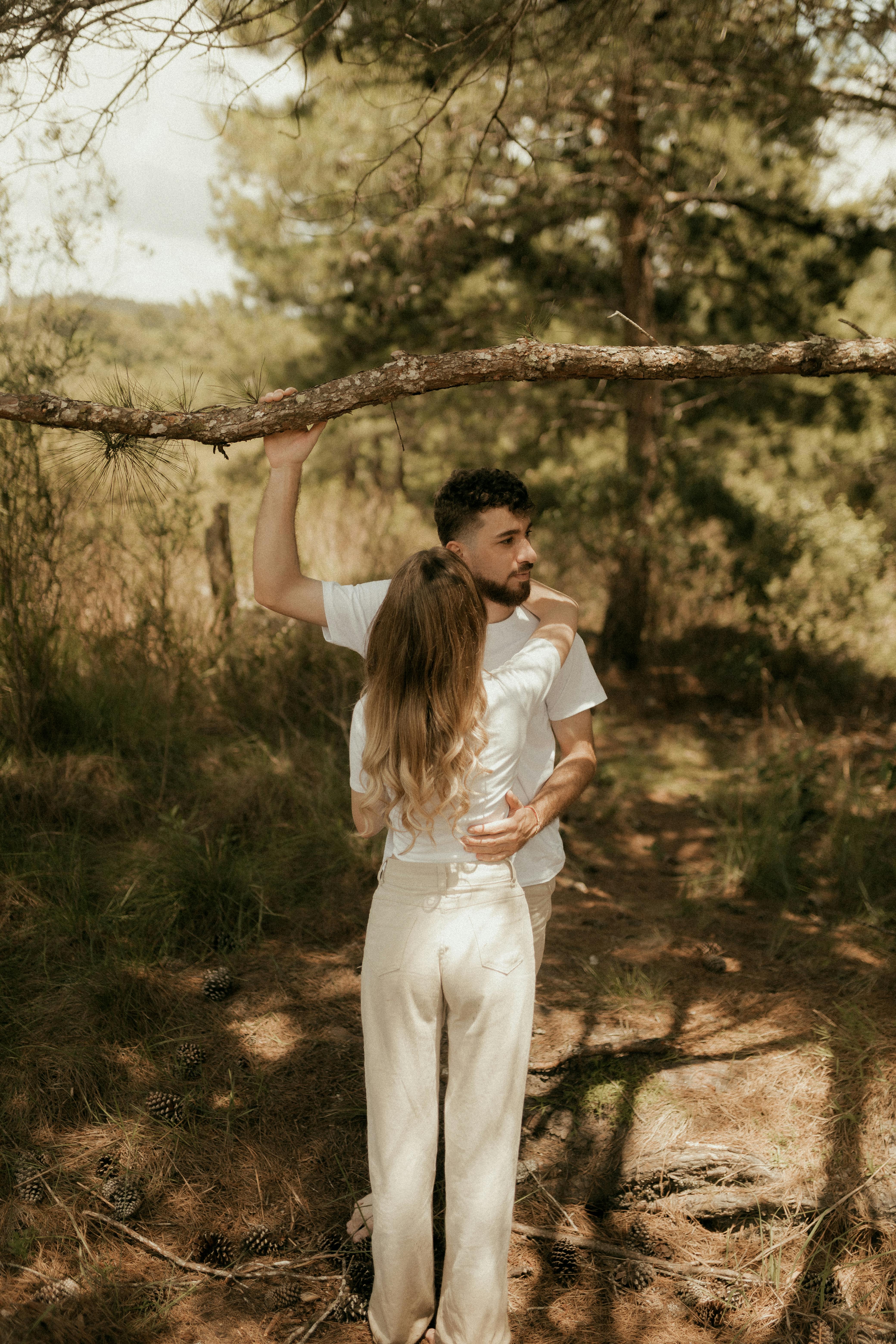 gratis Een romantisch stel omhelst elkaar in een zonovergoten bos, wat een sereen moment in de buitenlucht benadrukt. Stockfoto