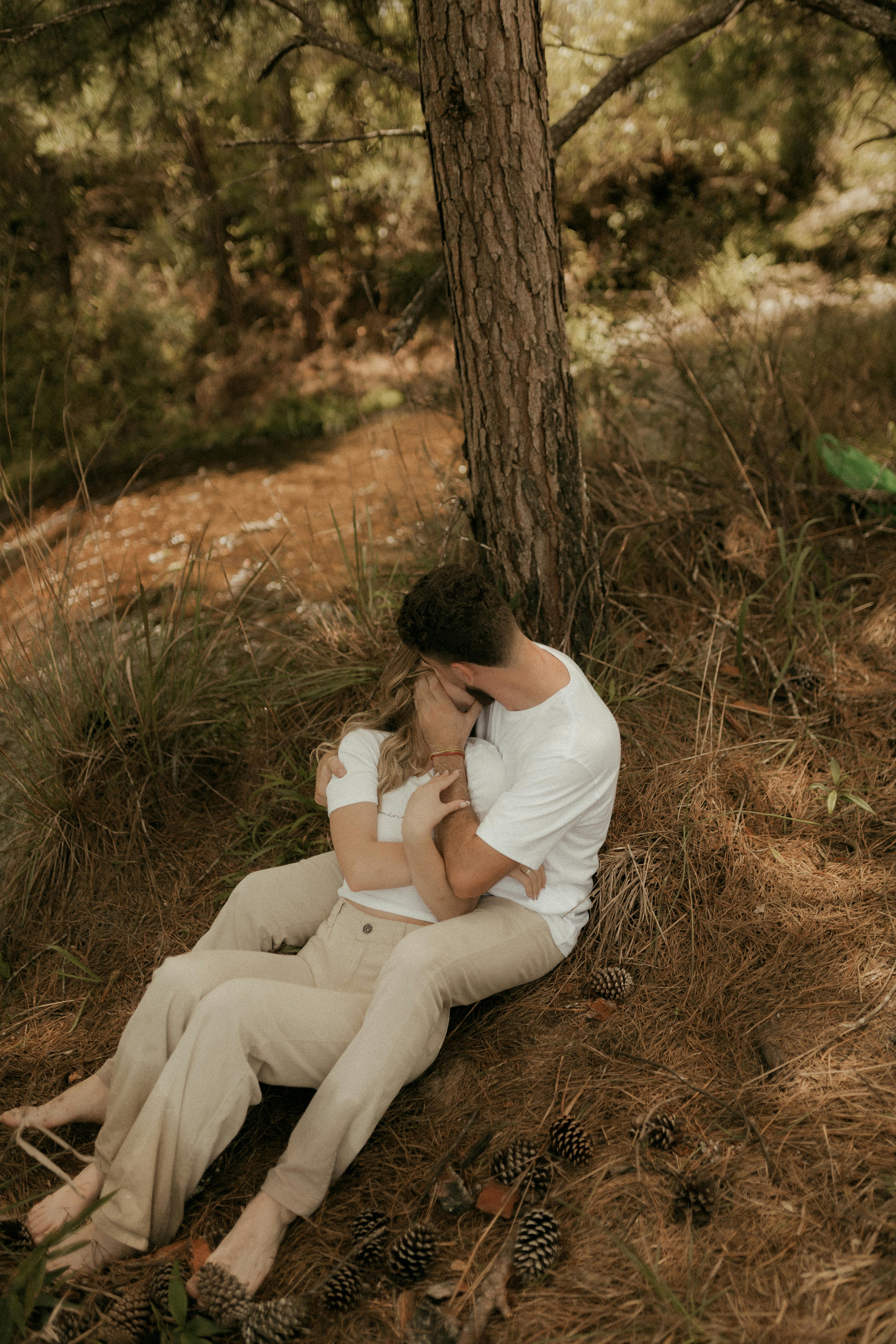 Gratis Sepasang kekasih berpelukan di bawah pohon, dikelilingi alam dengan suasana hangat. Foto Stok