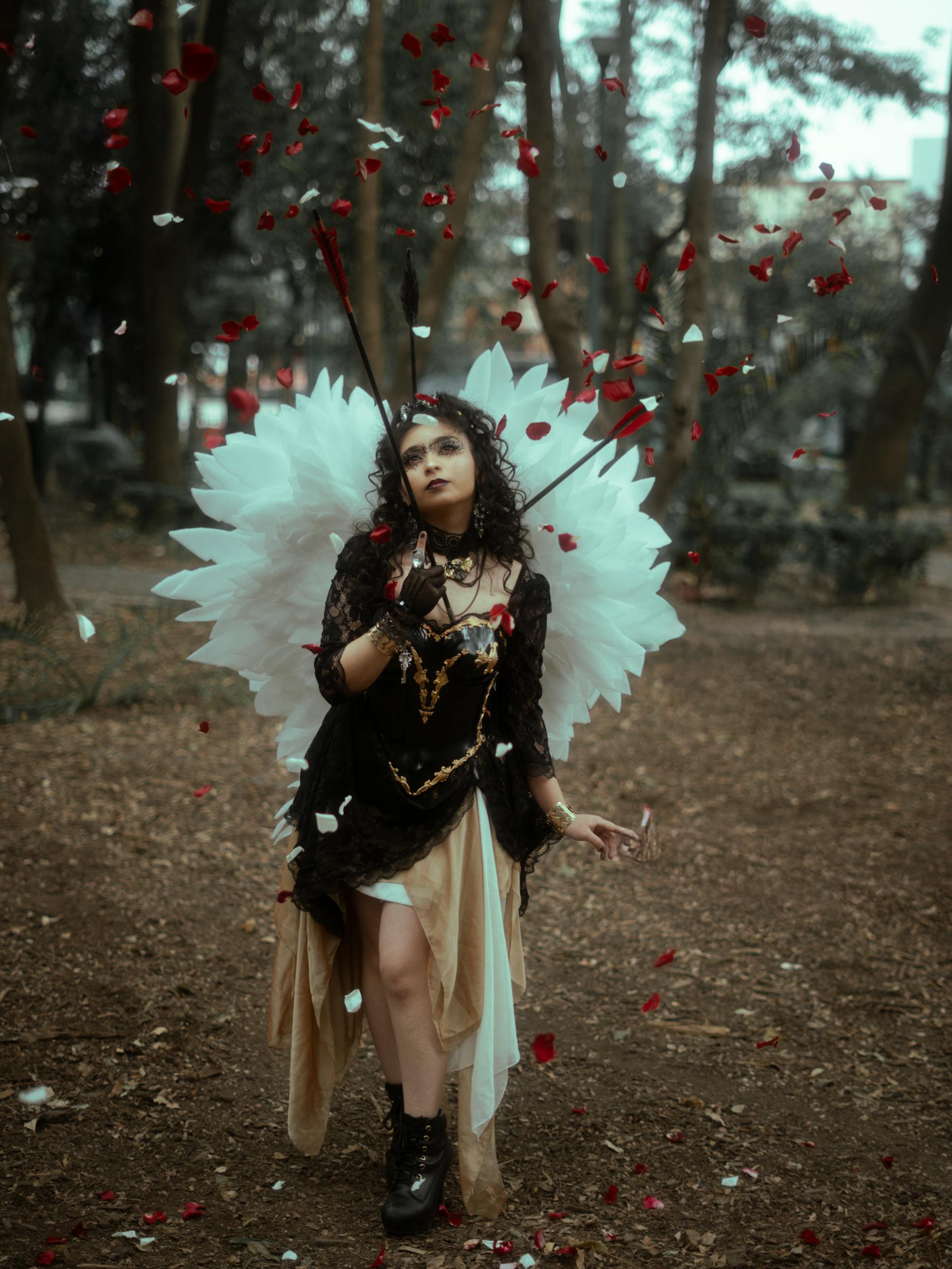 Gratis Una mujer misteriosa con atuendo angelical rodeada de pétalos de rosa flotantes en un bosque místico. Foto de stock