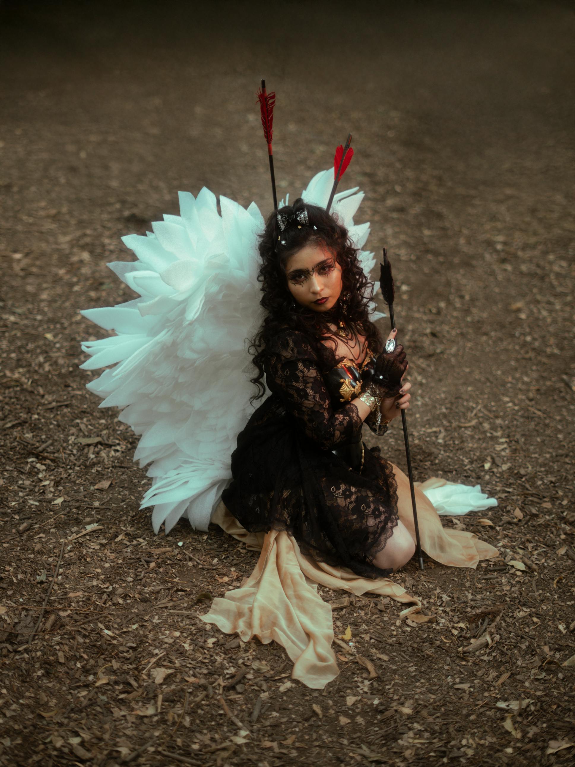 bezplatná Žena v kostýmu anděla s křídly klečící v lese, evokující fantasy témata. Základová fotografie