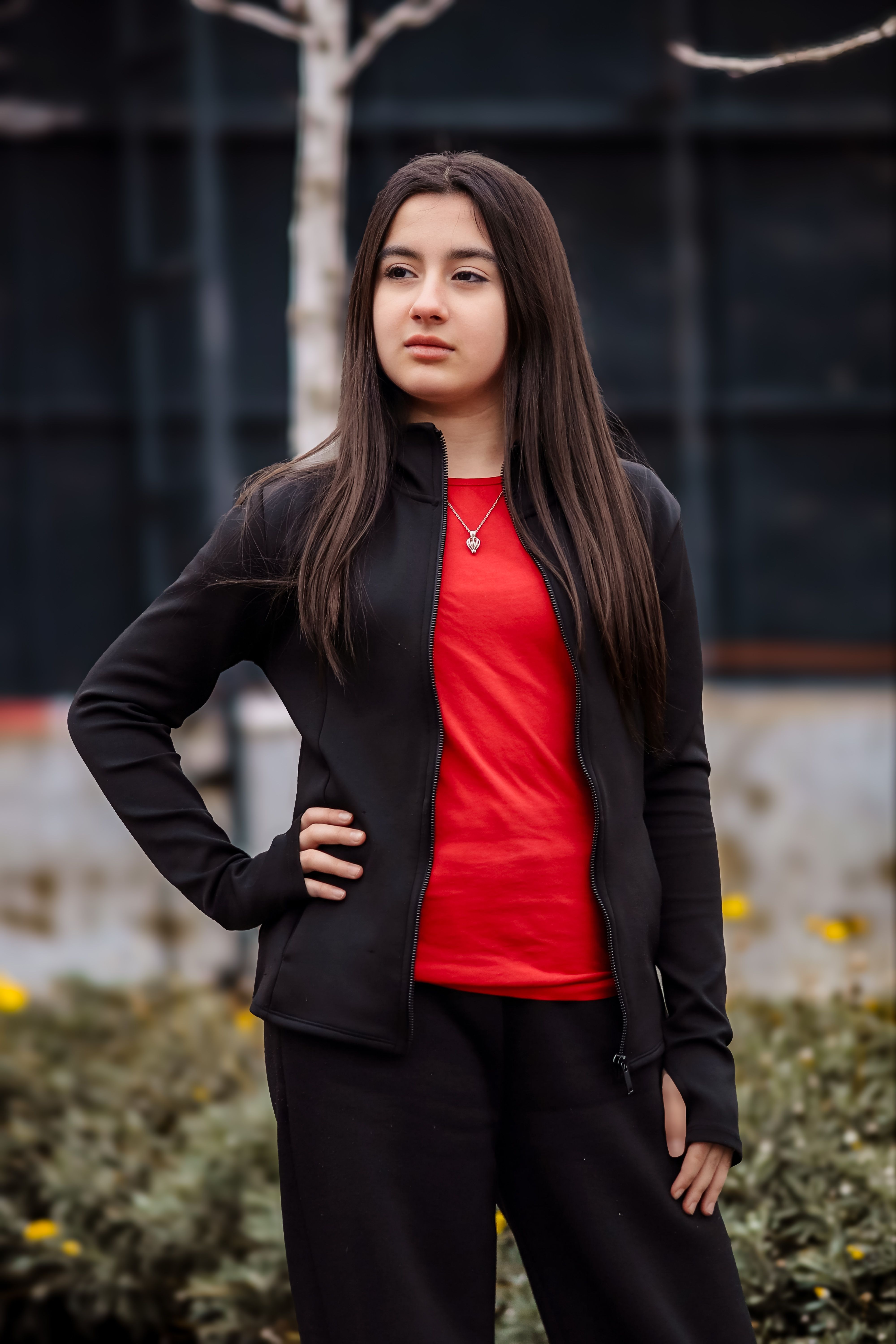 Portrait of a confident young woman standing outdoors in a casual outfit with a neutral expression.
