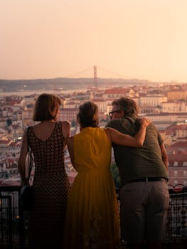 Three friends embracing as they overlook Lisbon's stunning skyline at sunset with the iconic 25 de Abril Bridge in the background.