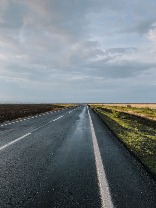 Free A straight, wet road extends towards the horizon under a cloudy sky, showcasing serenity and travel. Stock Photo