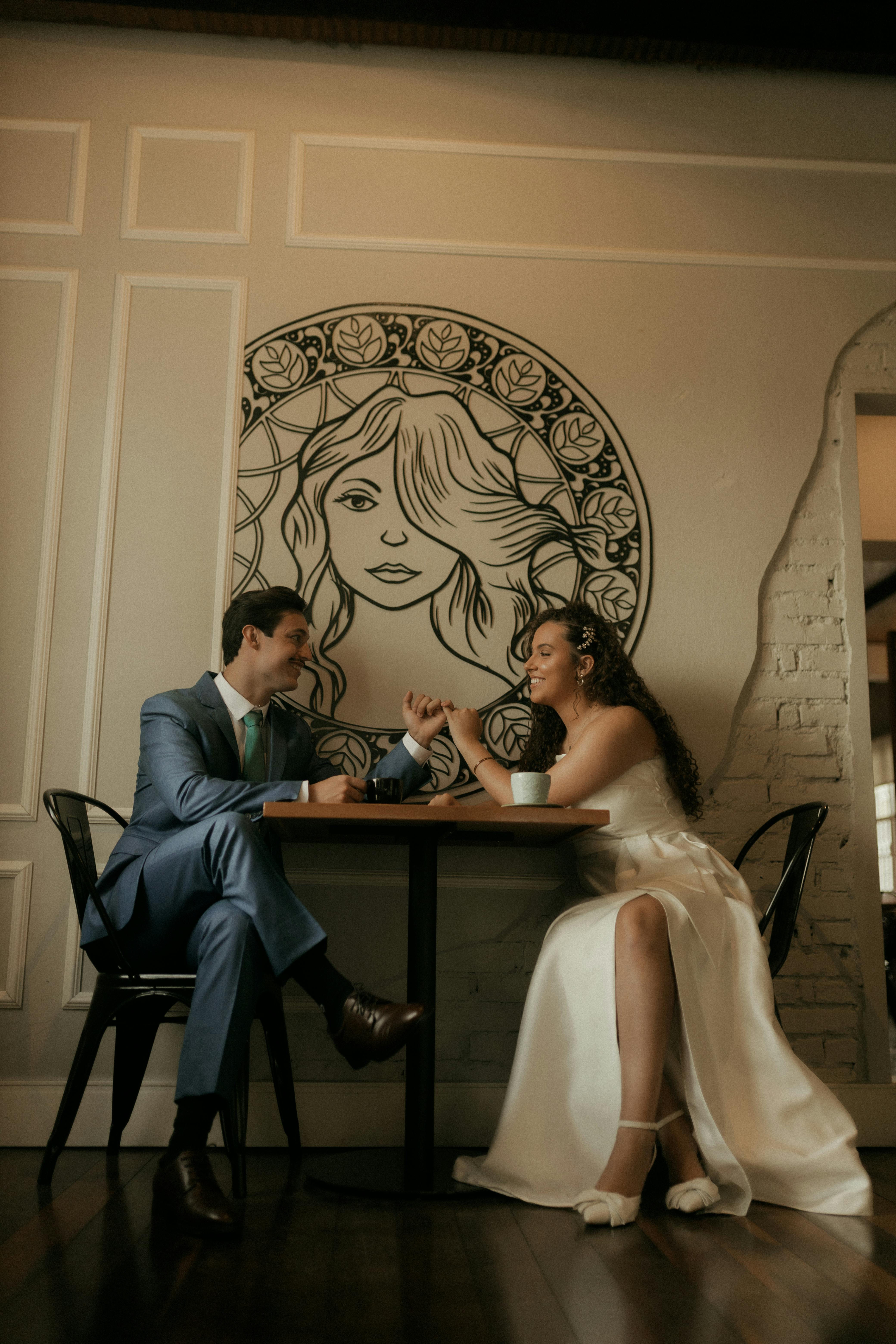 Gratis Par sitter ved bordet og nyter kaffe med en stilig veggmaleri i bakgrunnen. Arkivbilde