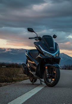 Black motorcycle parked on a scenic mountain road during sunset, showcasing sleek design and adventure.