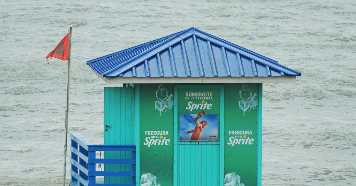 Bright lifeguard tower with advertisements on a cloudy day by the beach.