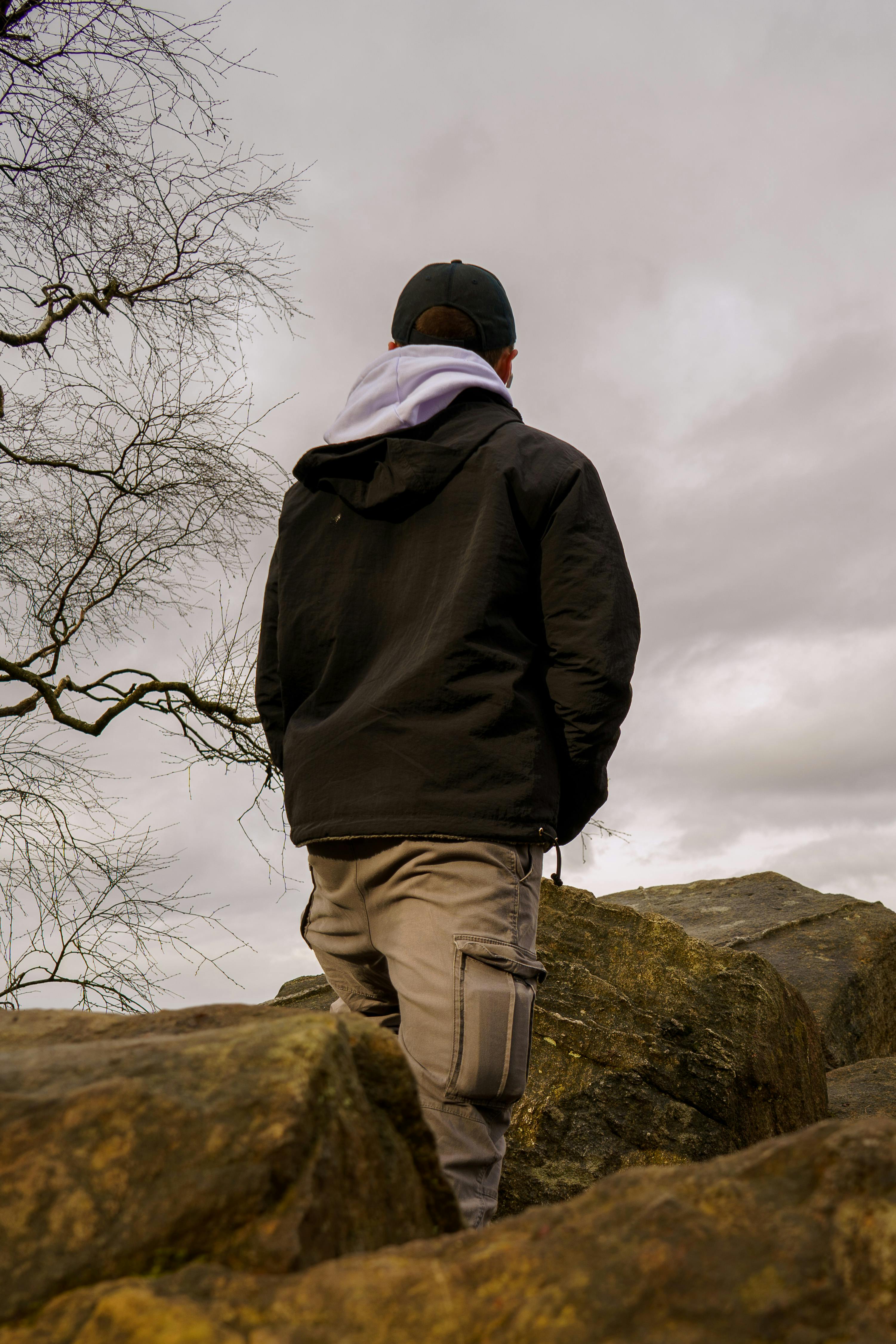 gratis Een man in vrijetijdskleding staat op rotsen onder een bewolkte hemel en staart in de verte. Stockfoto