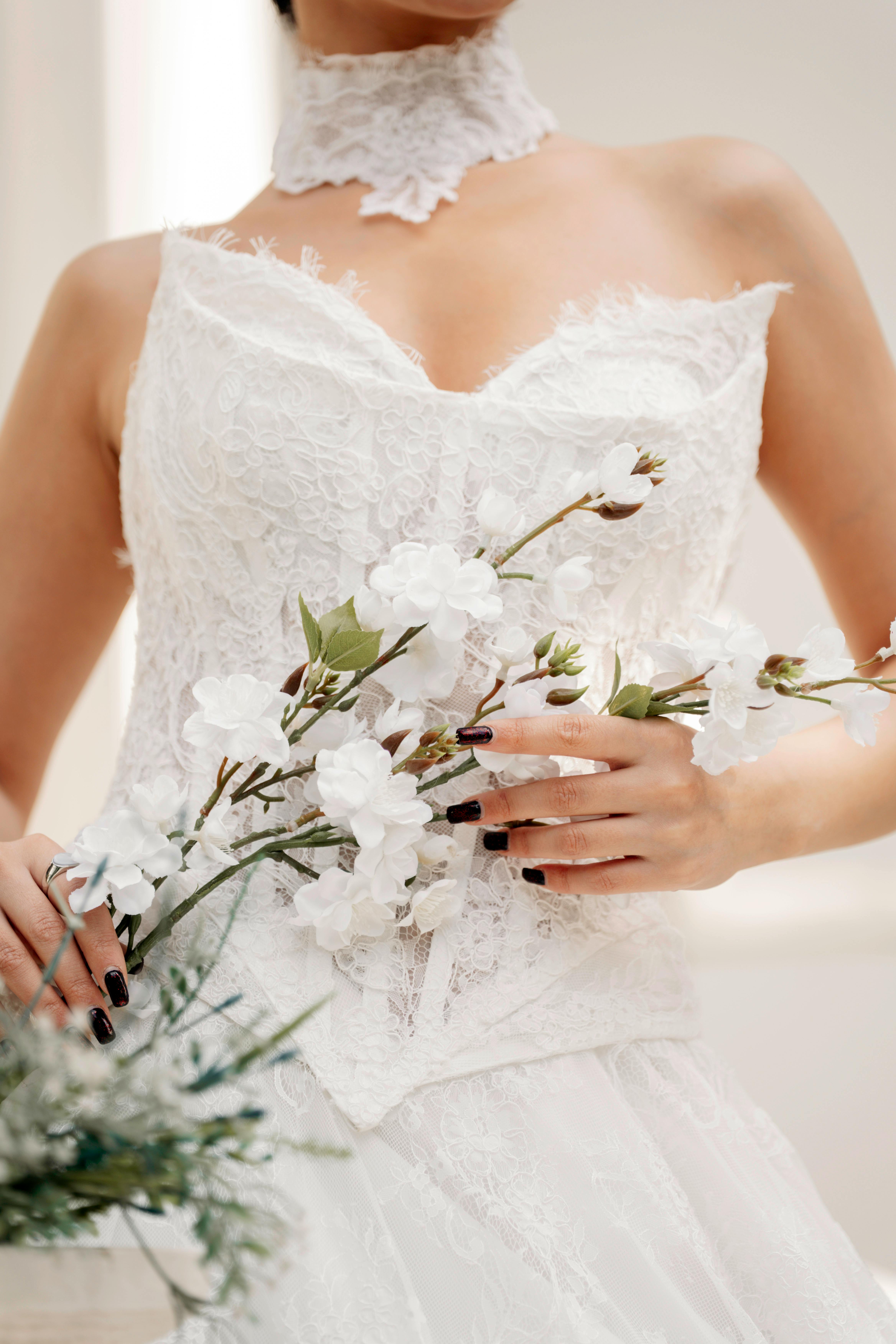 Gratis Primer plano de una novia con un vestido de novia de encaje sosteniendo un ramo de flores blancas, enfatizando la elegancia. Foto de stock