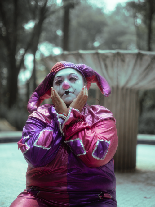 Free A colorful yet somber clown sits in a park, evoking deep emotions. Stock Photo