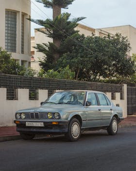 Vintage car parked by a suburban street with lush greenery and modern buildings.