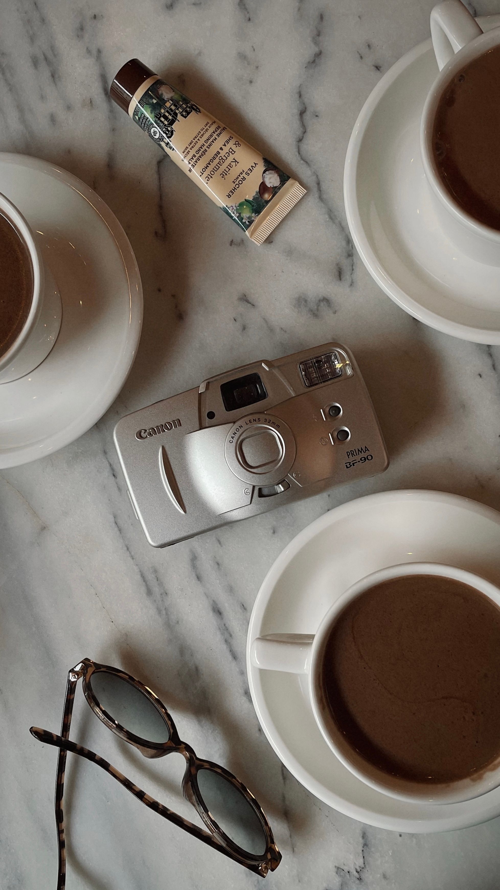 Flat Lay of Coffee, Camera, and Sunglasses on Marble · Free Stock Photo
