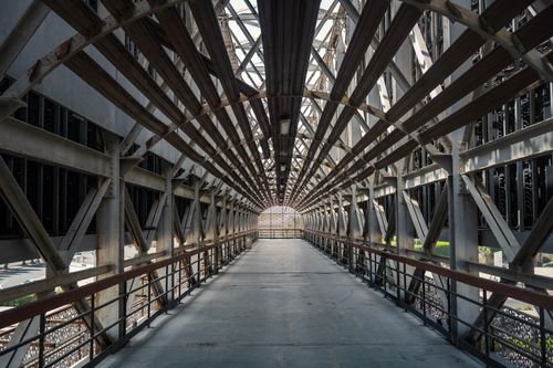 Free A symmetrical view of an industrial walkway adorned with intricate metal beams creating a geometric pattern. Stock Photo
