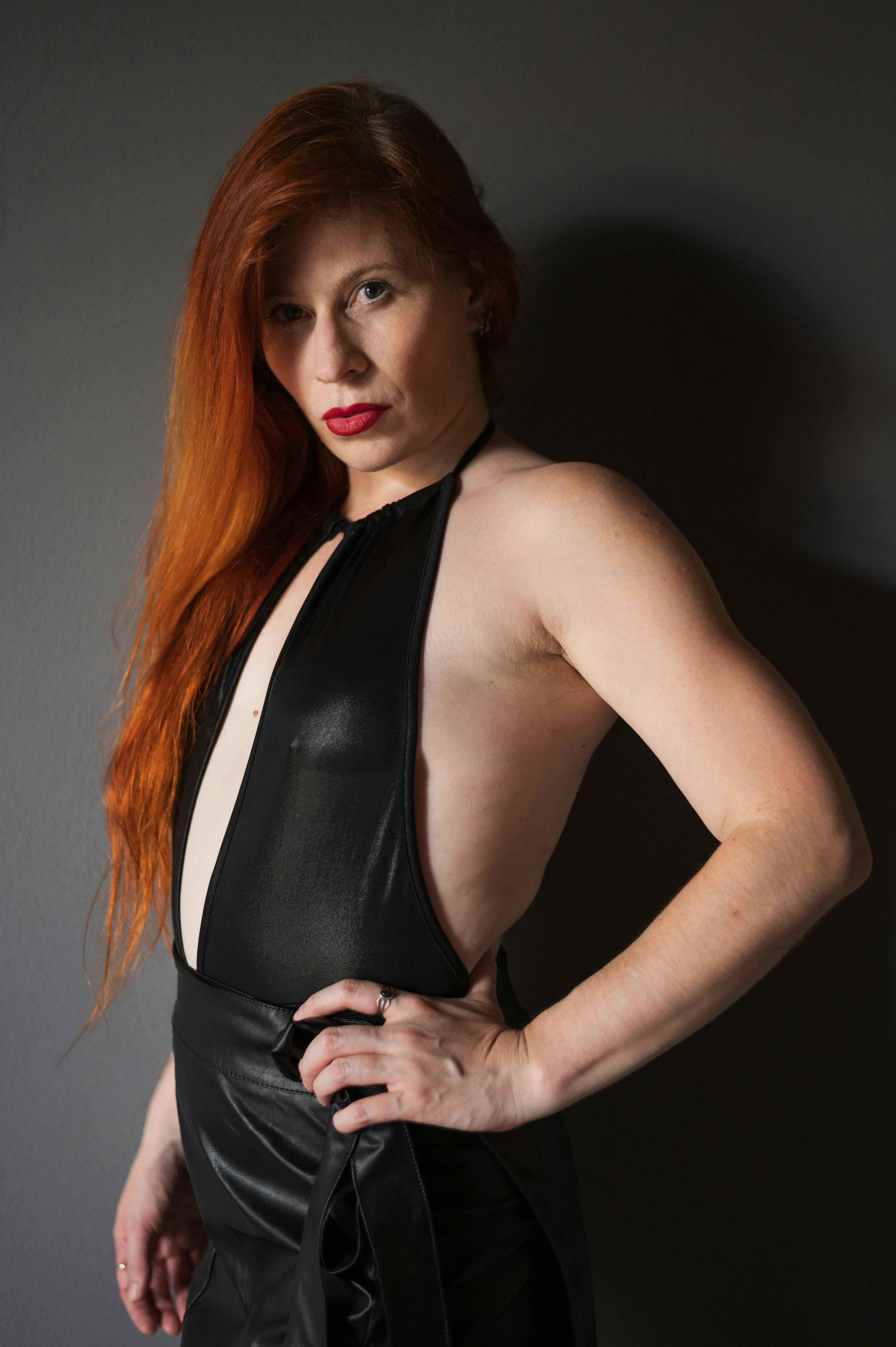 Kostenlos Porträt einer selbstbewussten Frau in einem schicken schwarzen Kleid mit roten Haaren, aufgenommen in einem Innenraum. Stock-Foto