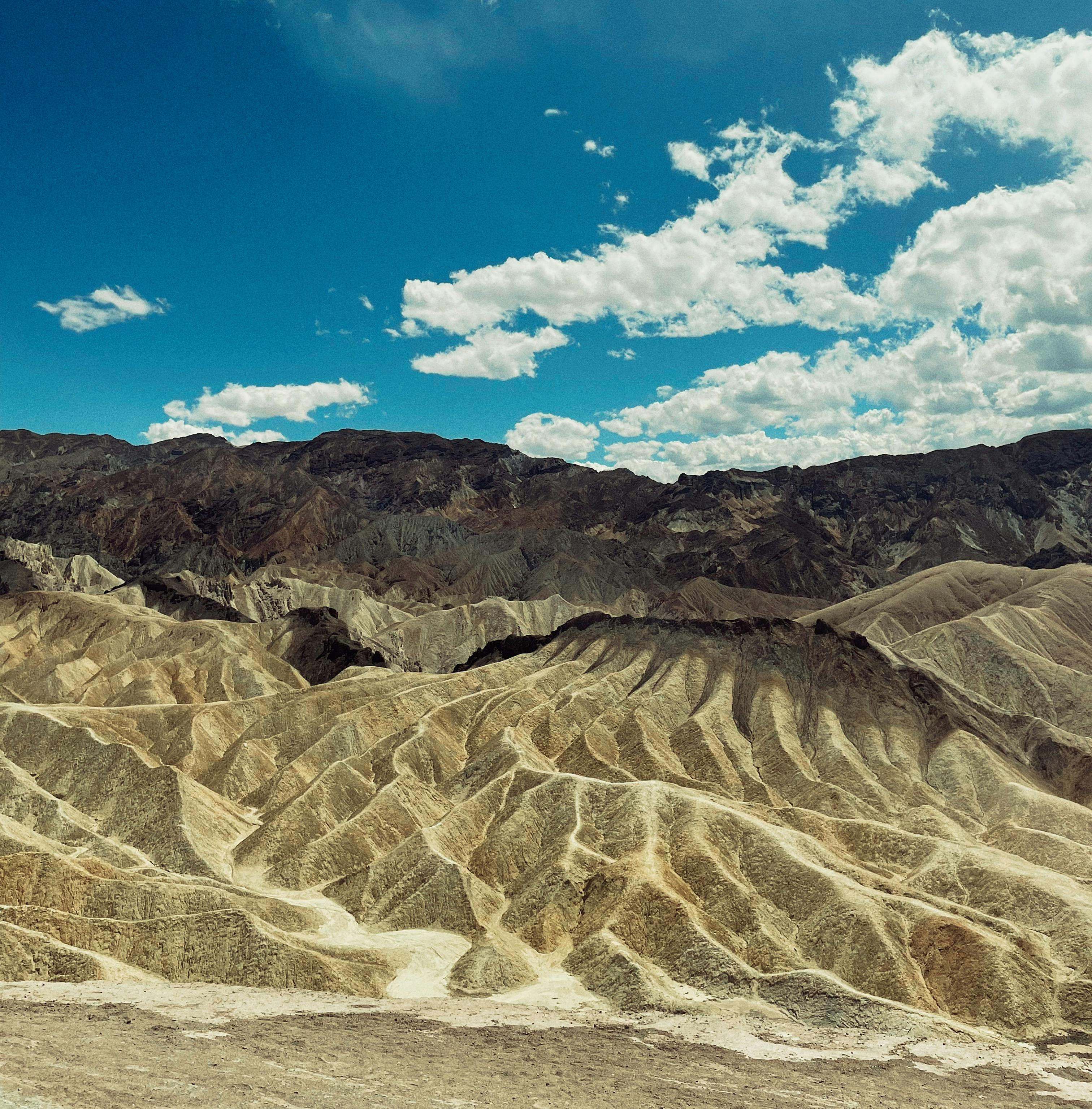 Ücretsiz Geniş, kurak bir arazi, masmavi gökyüzü ve dağınık bulutların altında eşsiz dağ oluşumlarıyla çevrili. Stok Fotoğraflar