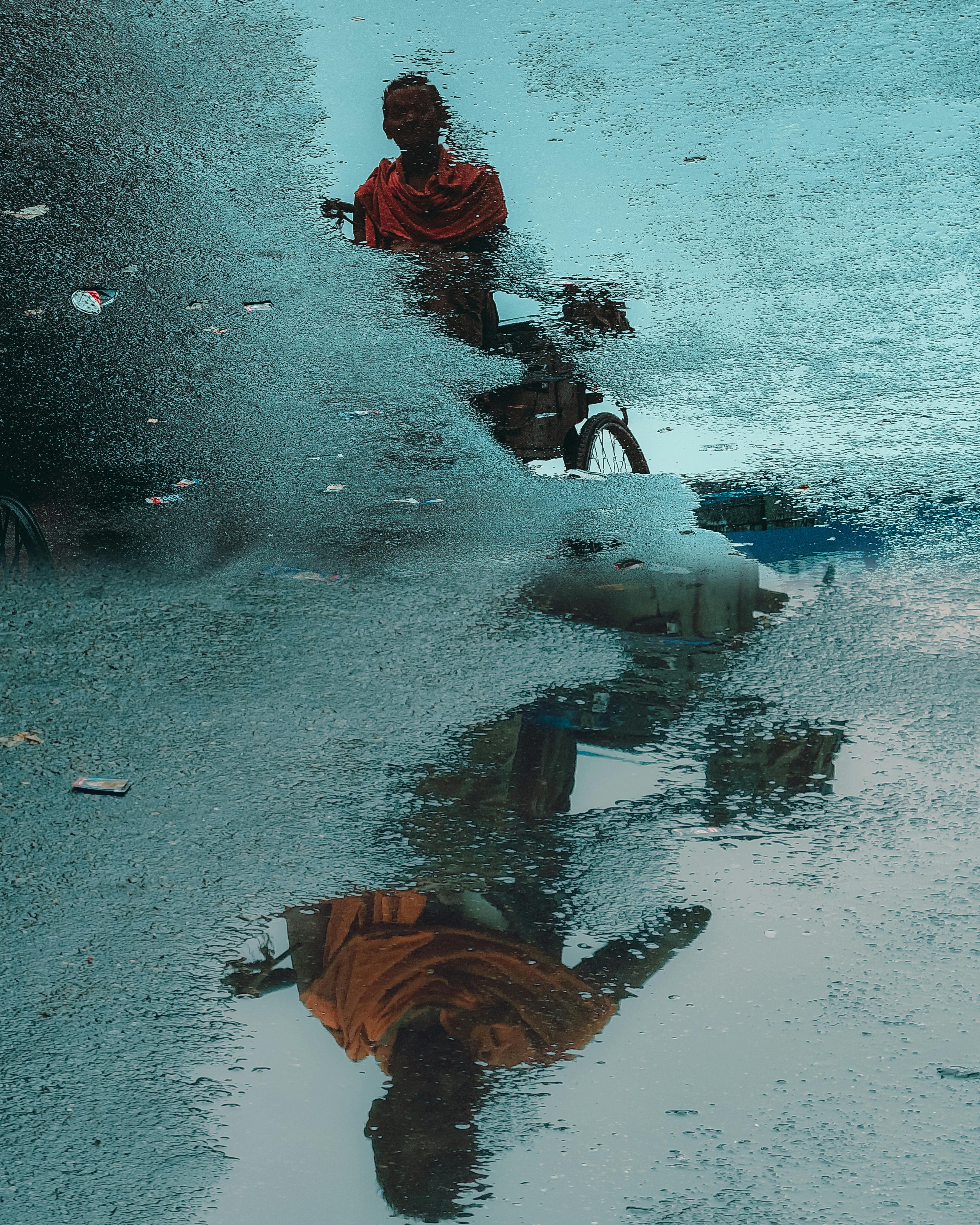 Gratis Riflesso di una persona in piedi accanto a una bicicletta in una pozzanghera d'acqua. Foto a disposizione