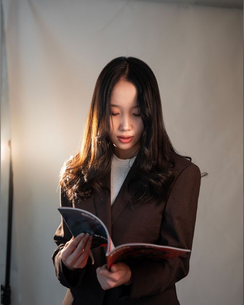 Free A young woman reading a magazine indoors in warm light, wearing a brown blazer. Stock Photo