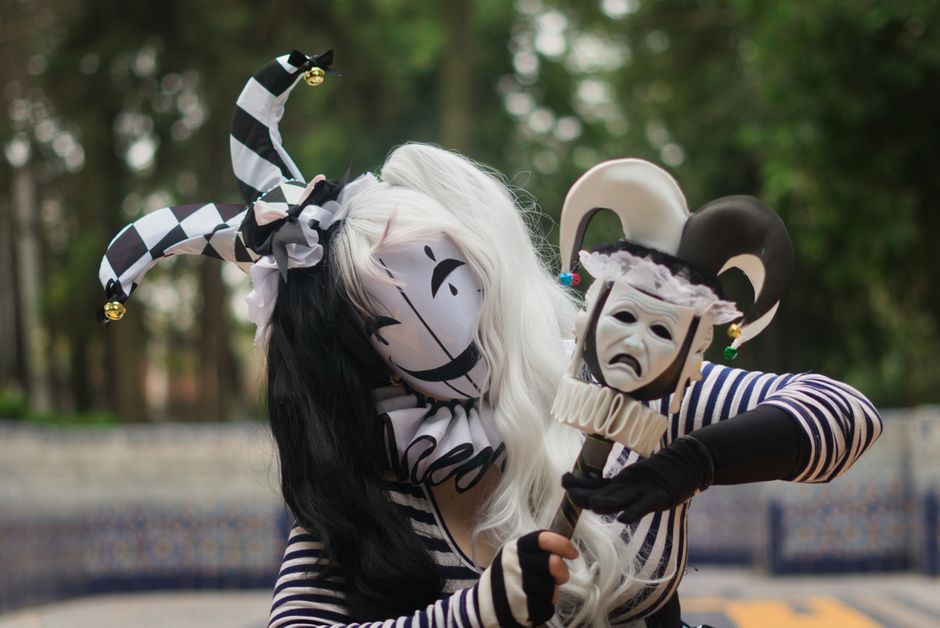 Close-up of a person in a whimsical jester costume outdoors holding a mask.