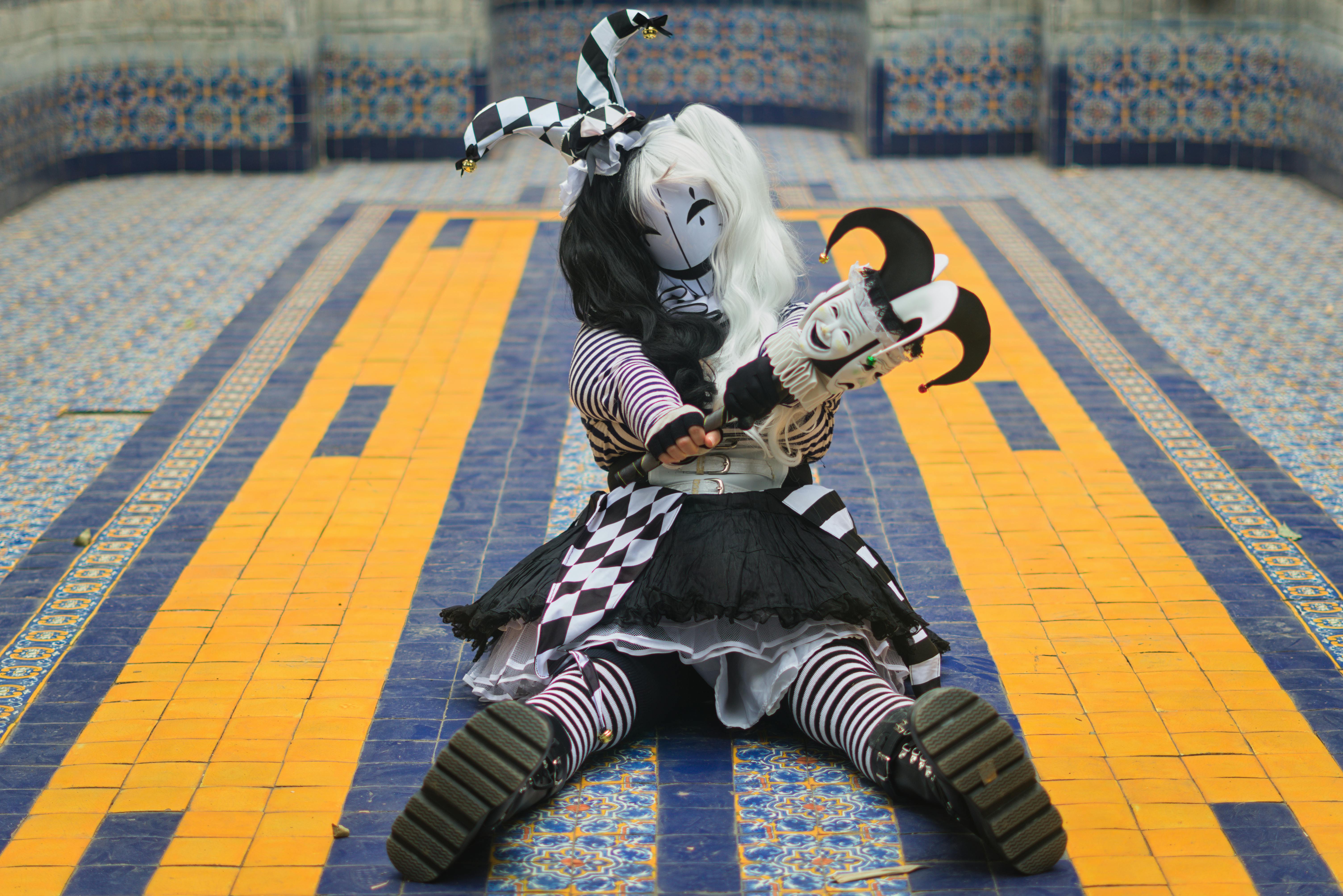 Gratis Un arlecchino vestito con un costume bianco e nero è seduto su un vivace pavimento piastrellato a mosaico. Foto a disposizione