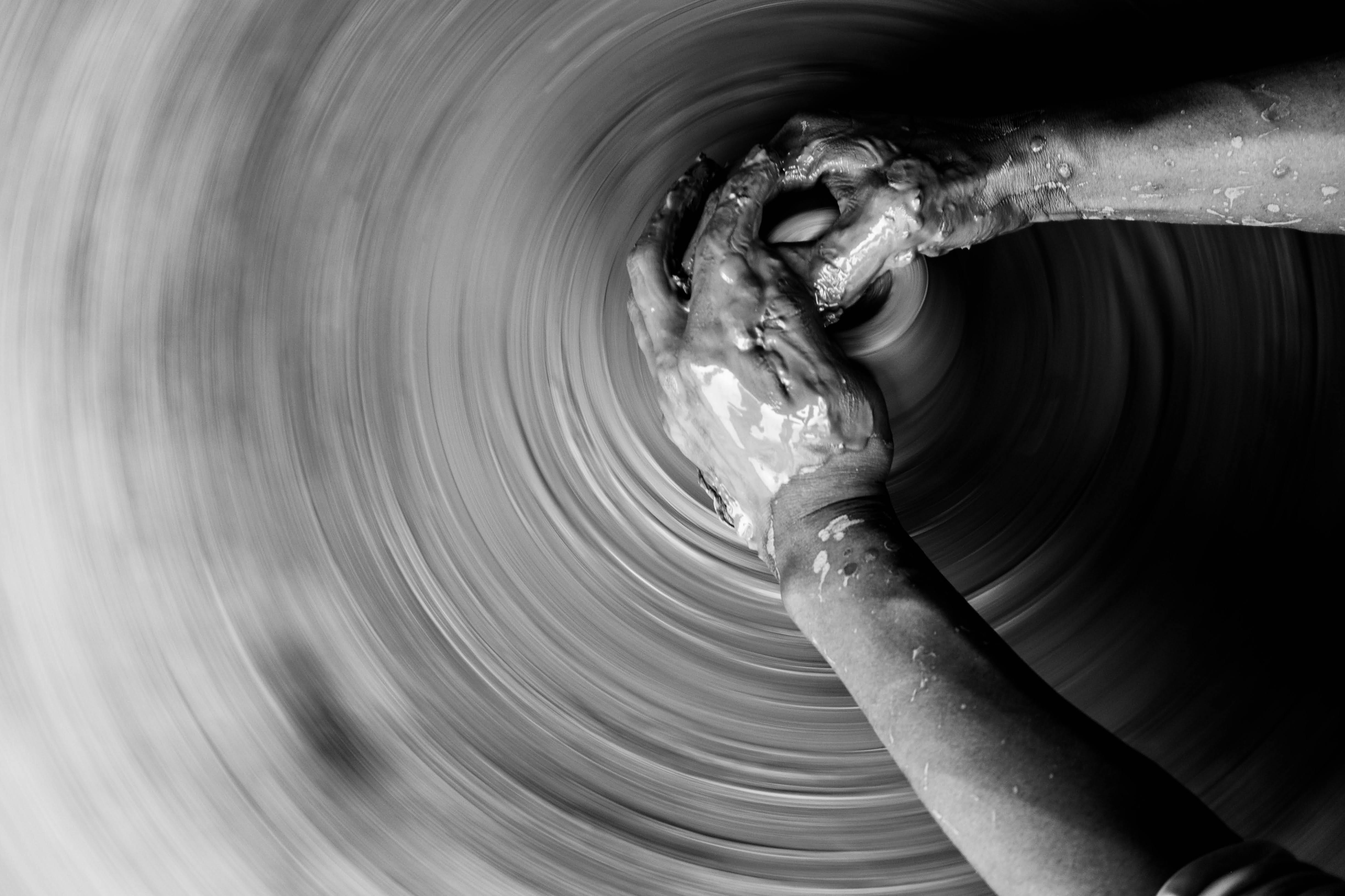 Gratis Primer plano en blanco y negro de manos elaborando cerámica en una rueca, capturando la habilidad y la fluidez artesanal. Foto de stock