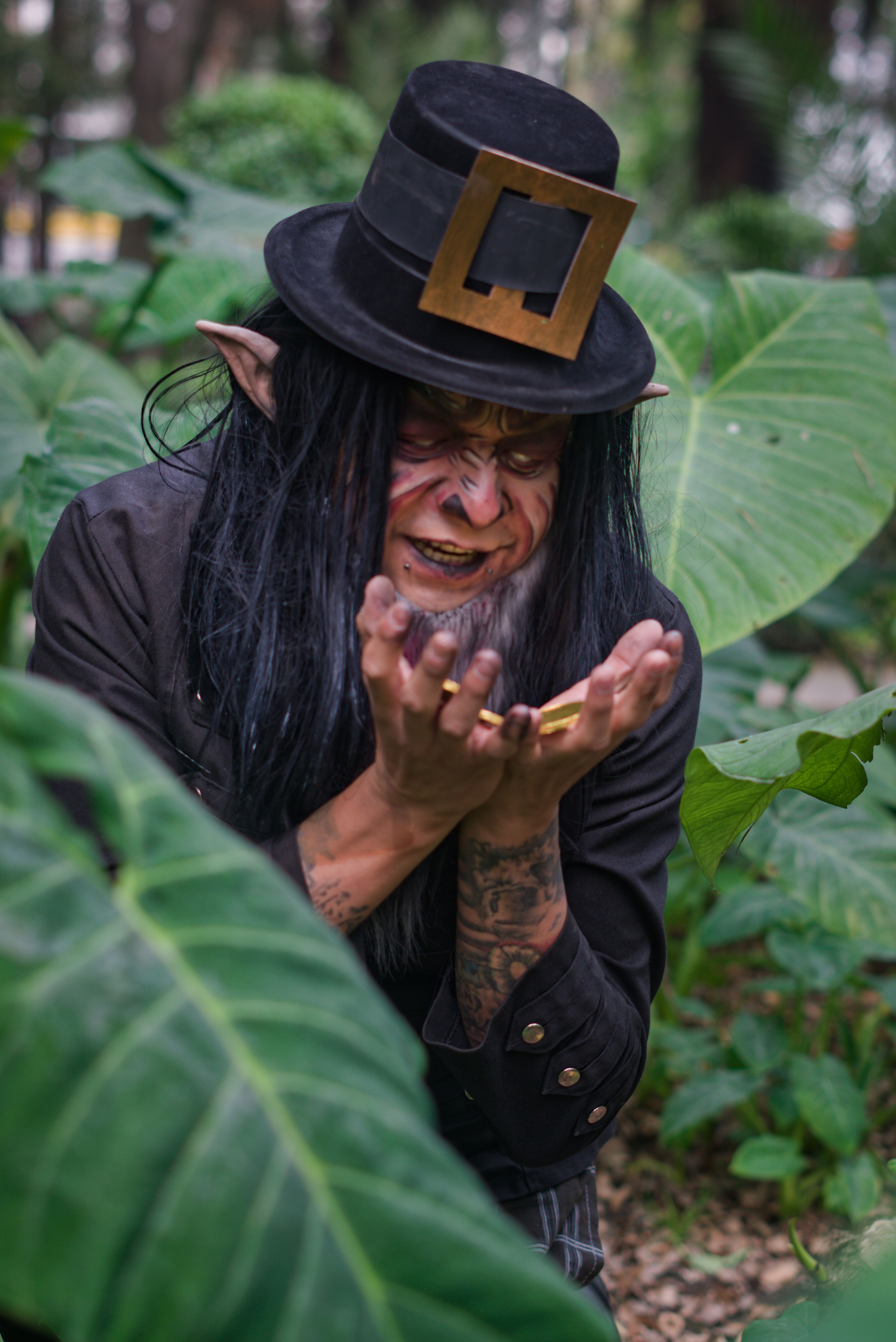 Leprechaun with hat and ears smiling mischievously outdoors in lush foliage.