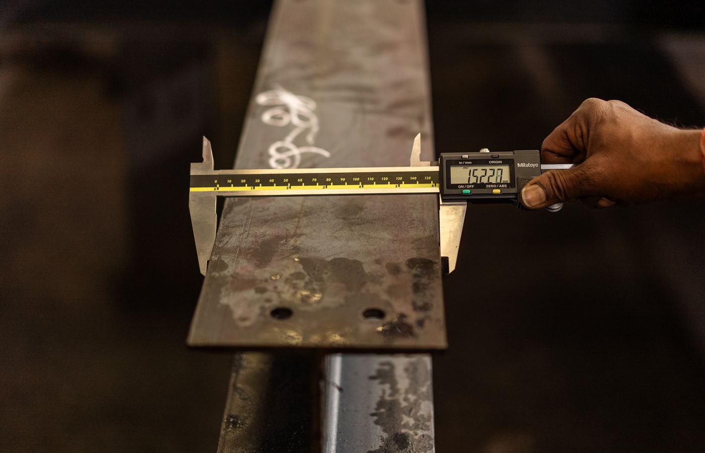 Quality inspector measuring a steel component with a digital caliper in an industrial workshop