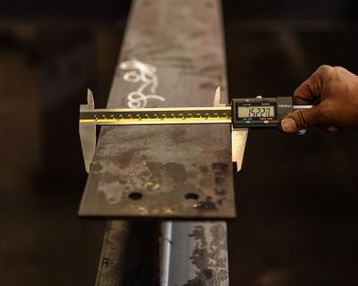 Worker measuring a metal part with a digital caliper for quality inspection