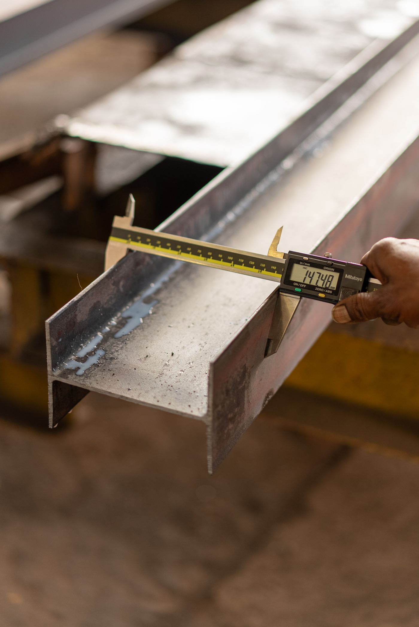 Caliper measuring a steel beam flange — dimensional check before dispatch
