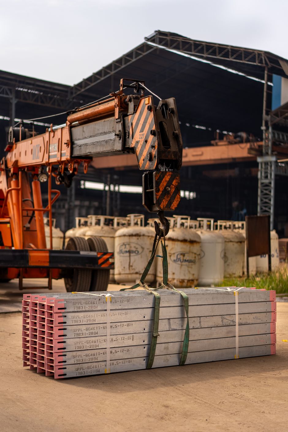 Industrial scene with crane lifting metal beams at a factory location.