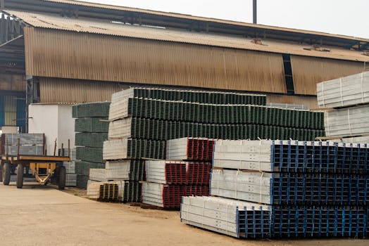 Outdoor view of an industrial warehouse with multiple stacks of metal beams and pallets.
