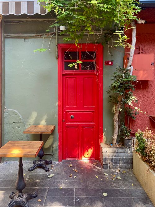 Free A stunning red door on a quaint street in Istanbul, surrounded by plants and outdoor seating. Stock Photo