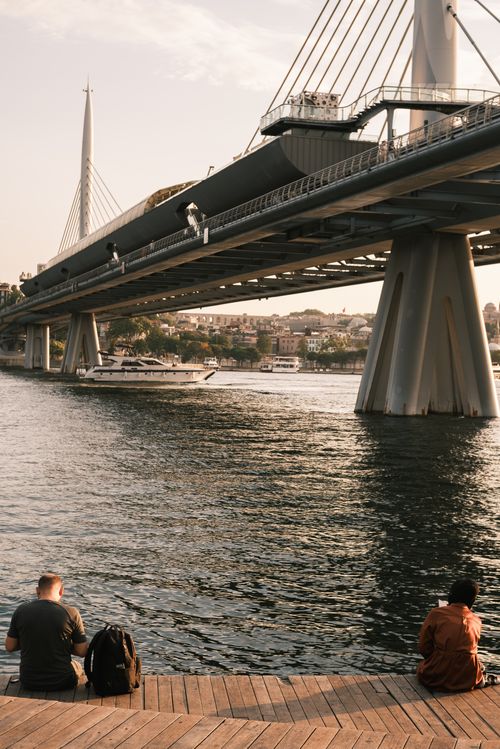 Free People relaxing by the water under a striking cable-stayed bridge at sunset in Istanbul. Stock Photo