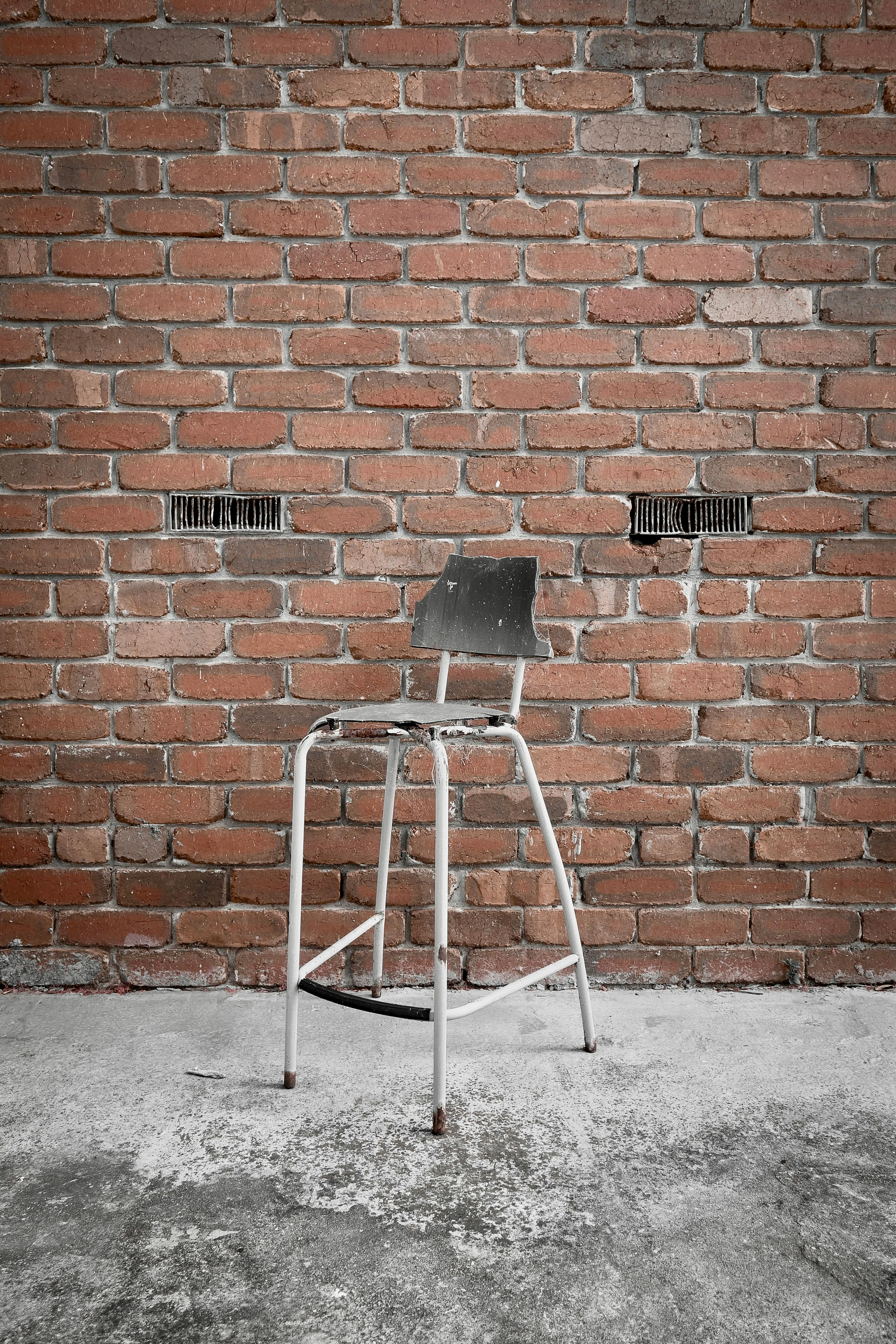 grátis Uma velha cadeira de metal encostada em uma parede de tijolos cria um ambiente rústico. Foto profissional