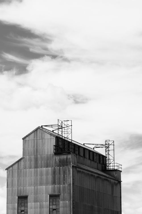 Free Black and white image of an industrial warehouse against a moody sky. Stock Photo