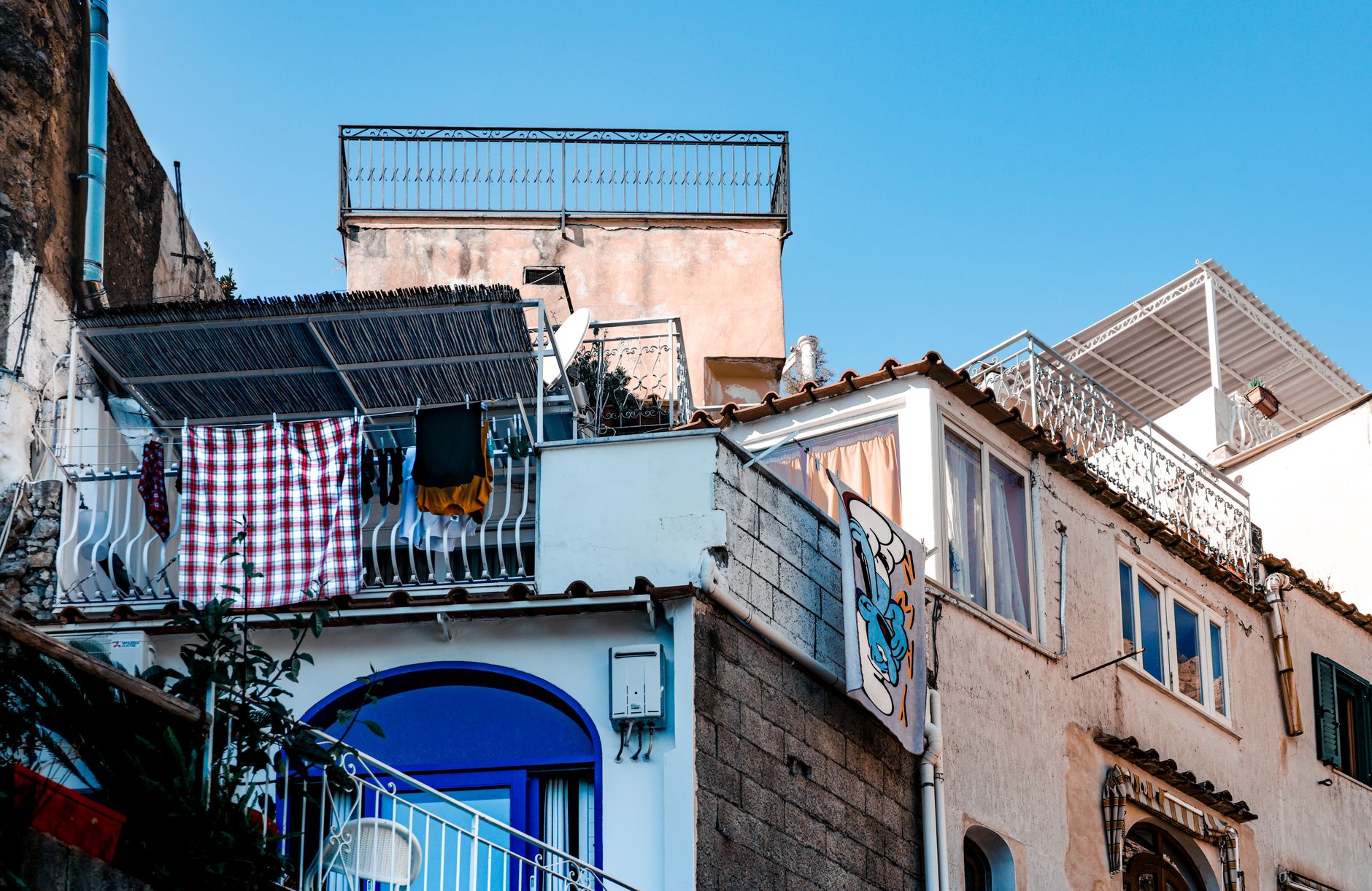 A quaint Mediterranean apartment building with laundry hanging on the balcony against a bright blue sky.