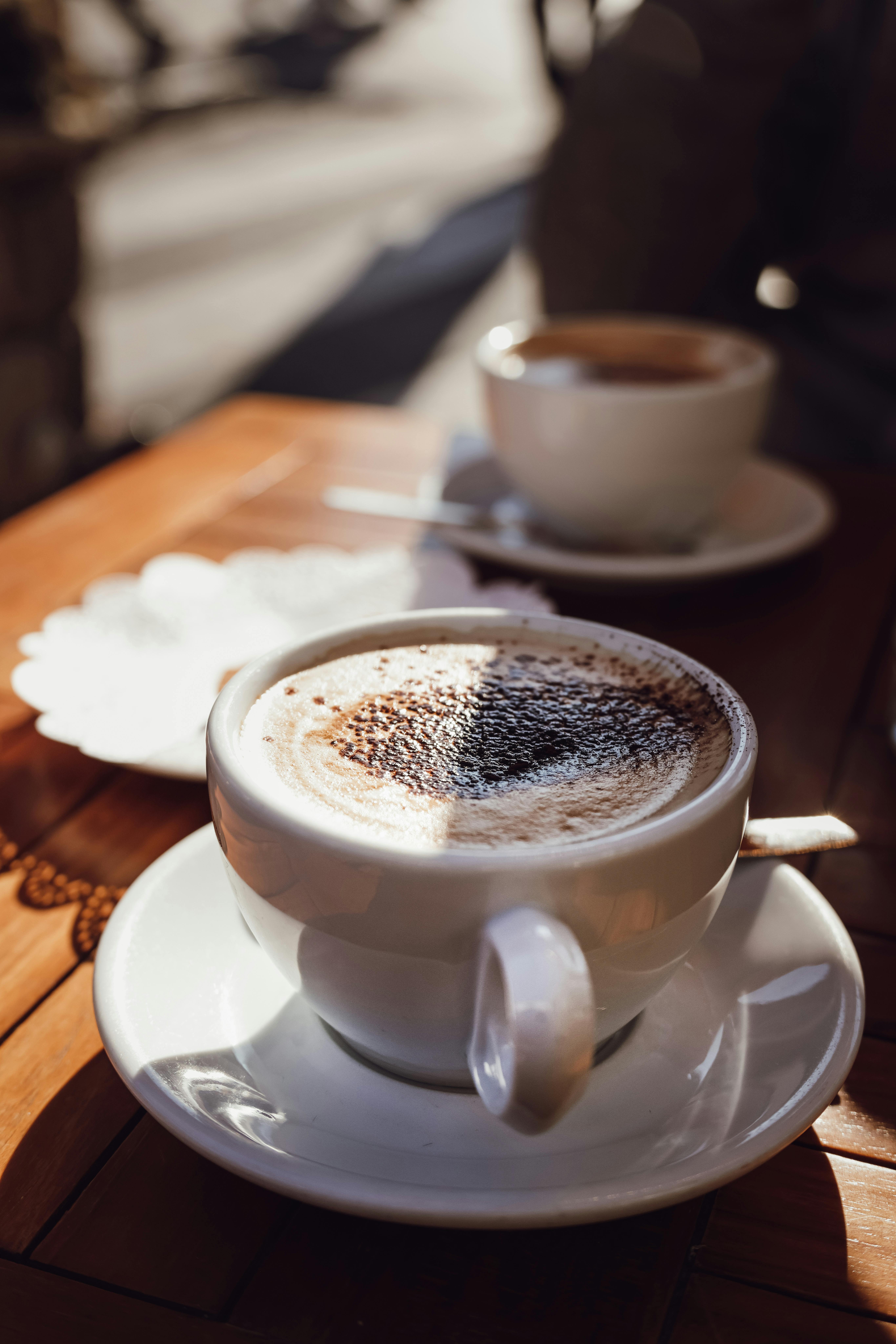 Miễn phí Những tách cappuccino ấm áp đặt trên chiếc bàn cà phê ngoài trời ngập nắng, mời gọi sự thư giãn. Ảnh lưu trữ