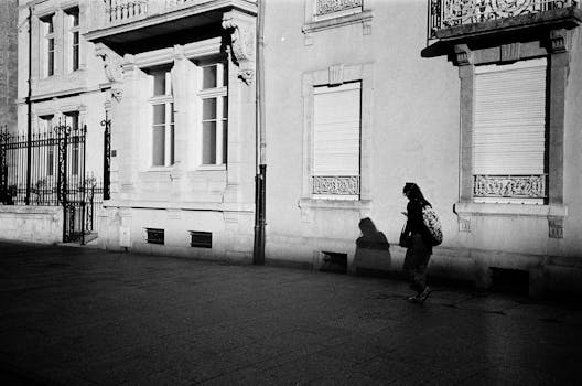 Vintage street scene featuring a lone walker in Nancy, France, with strong shadows against classic architecture.