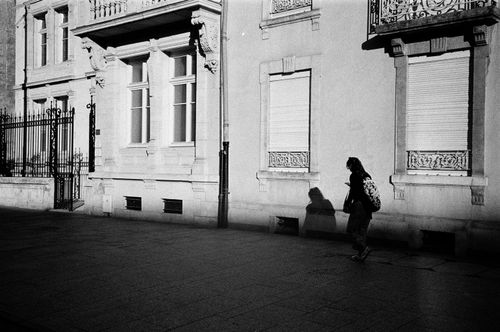 Free Vintage street scene featuring a lone walker in Nancy, France, with strong shadows against classic architecture. Stock Photo