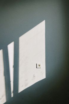 Artistic shadow of window light on a wall with a light switch, creating a minimalist mood.