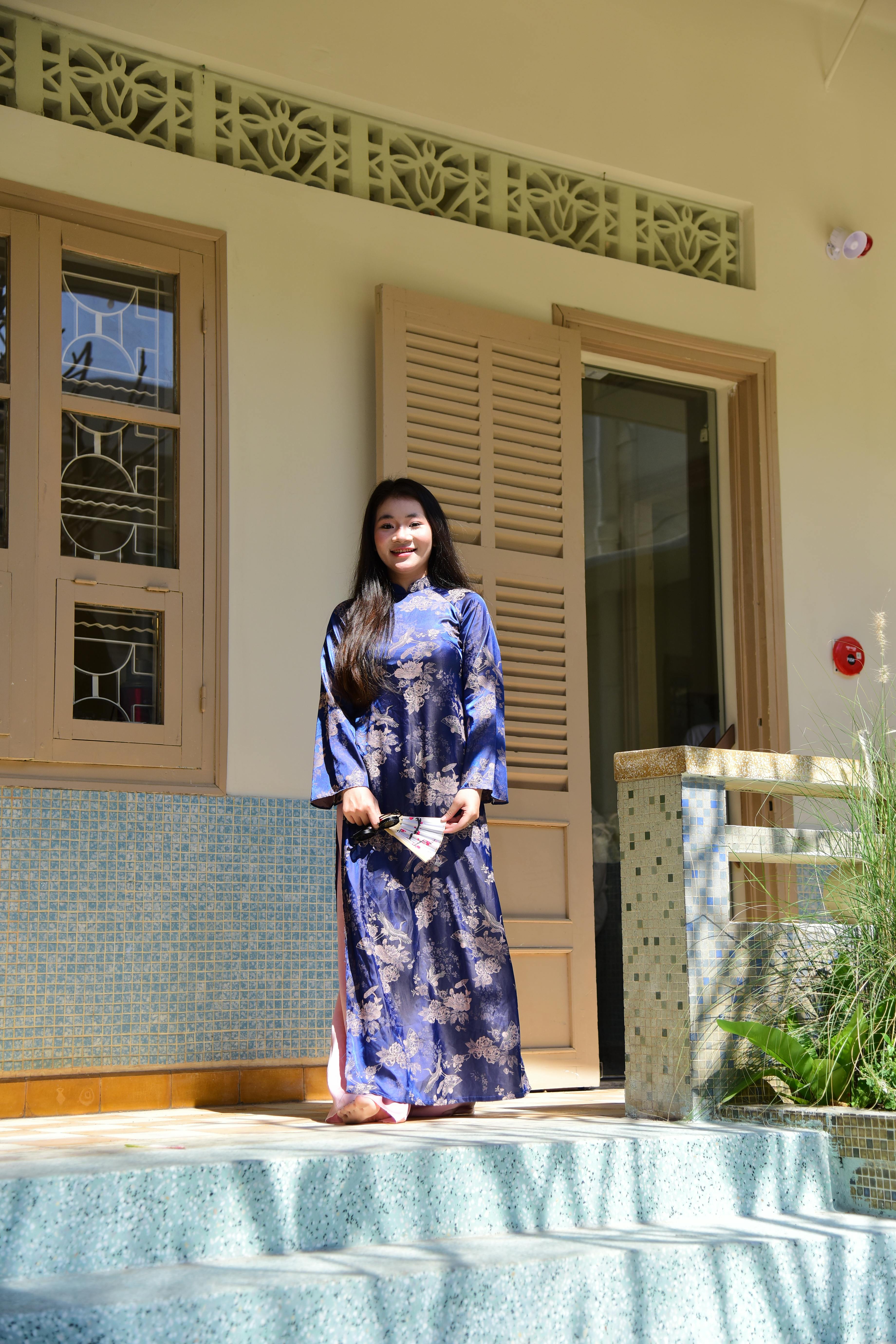 Ücretsiz Güneşli bir günde, geleneksel Vietnam kıyafeti olan áo dài giymiş genç bir kadın kapı aralığında duruyor. Stok Fotoğraflar