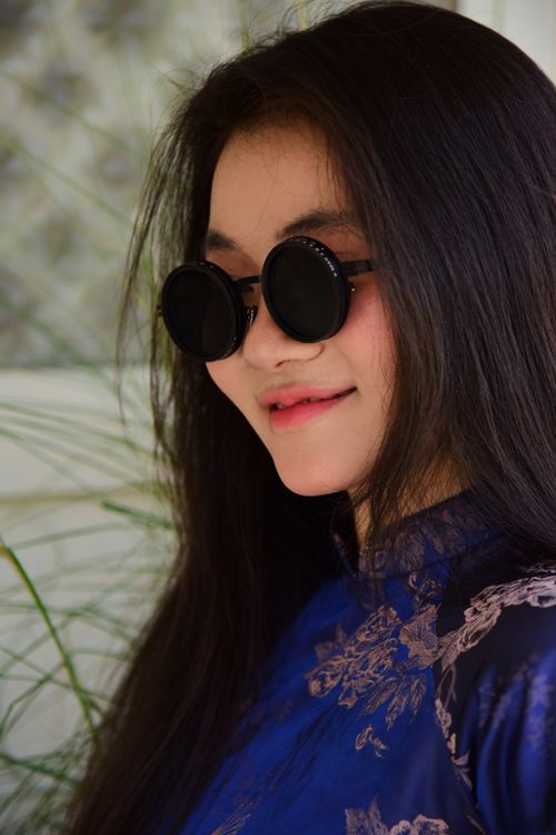Free Portrait of a woman wearing round sunglasses and a floral-patterned blue dress. Stock Photo