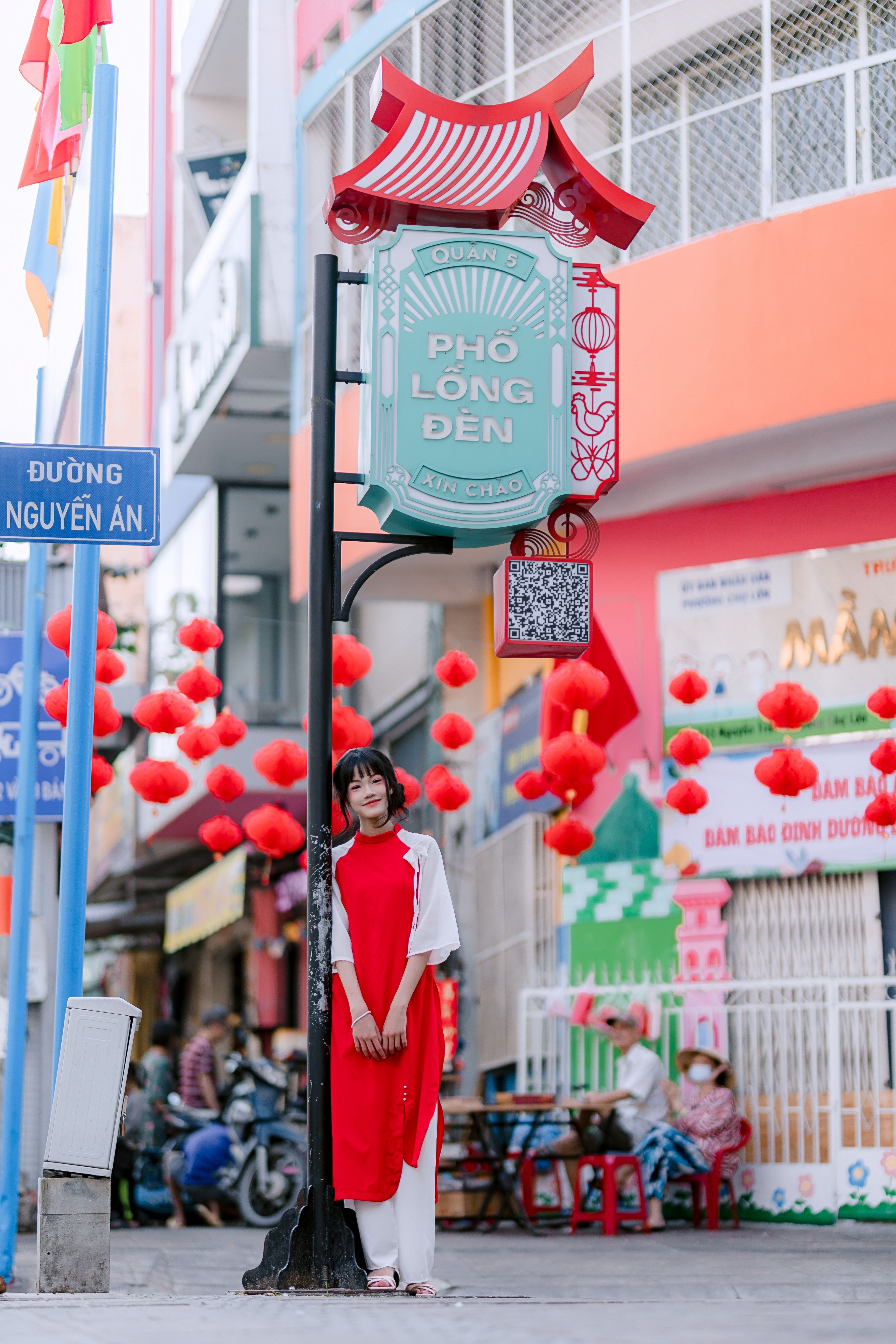 Young woman in traditional Vietnamese dress standing on Phố Lồng Đèn street. Bright, festive scene with red lanterns.