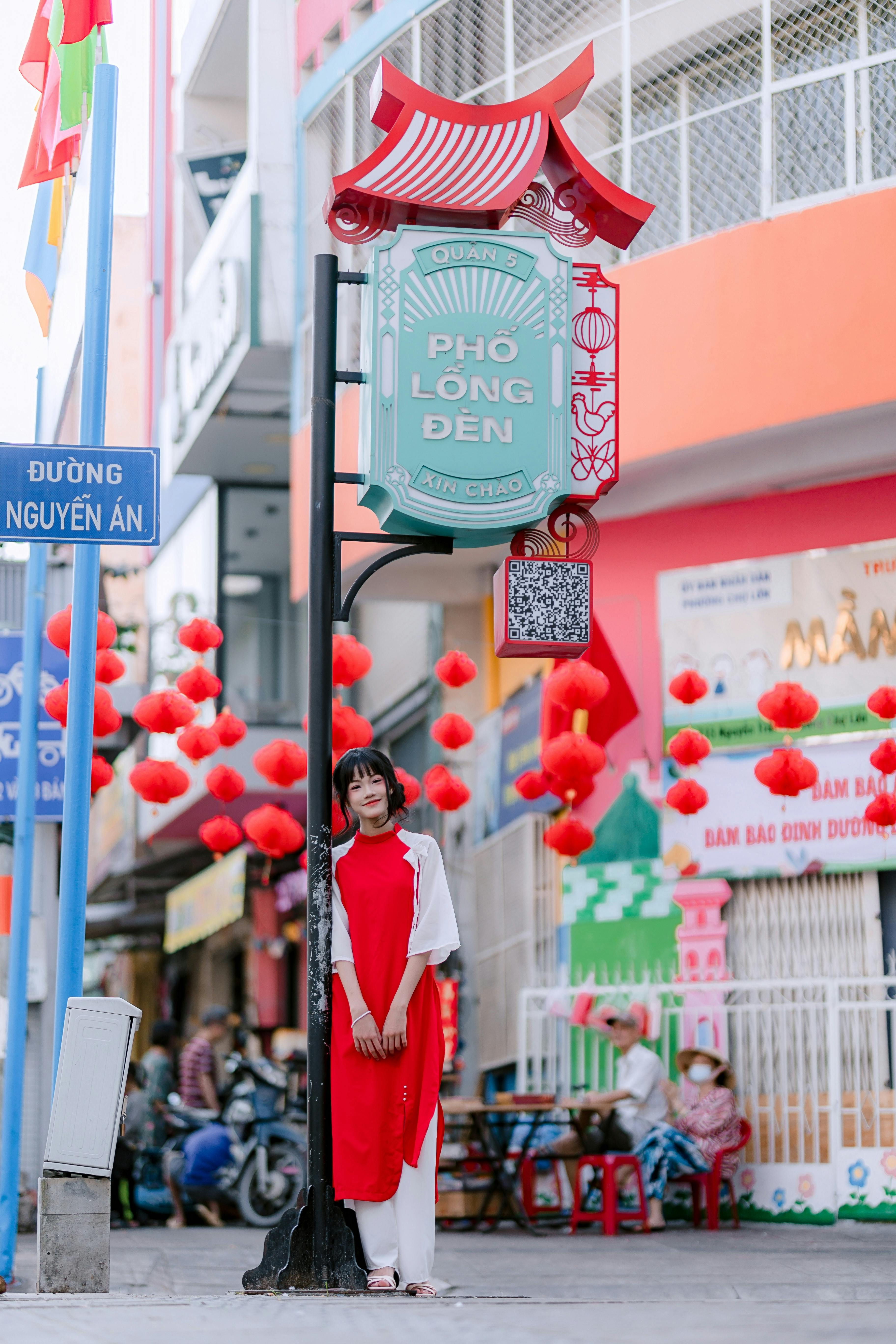 Ücretsiz Phố Lồng Đèn caddesinde geleneksel Vietnam kıyafetleri giymiş genç bir kadın duruyor. Kırmızı fenerlerle ışıl ışıl, şenlikli bir manzara. Stok Fotoğraflar