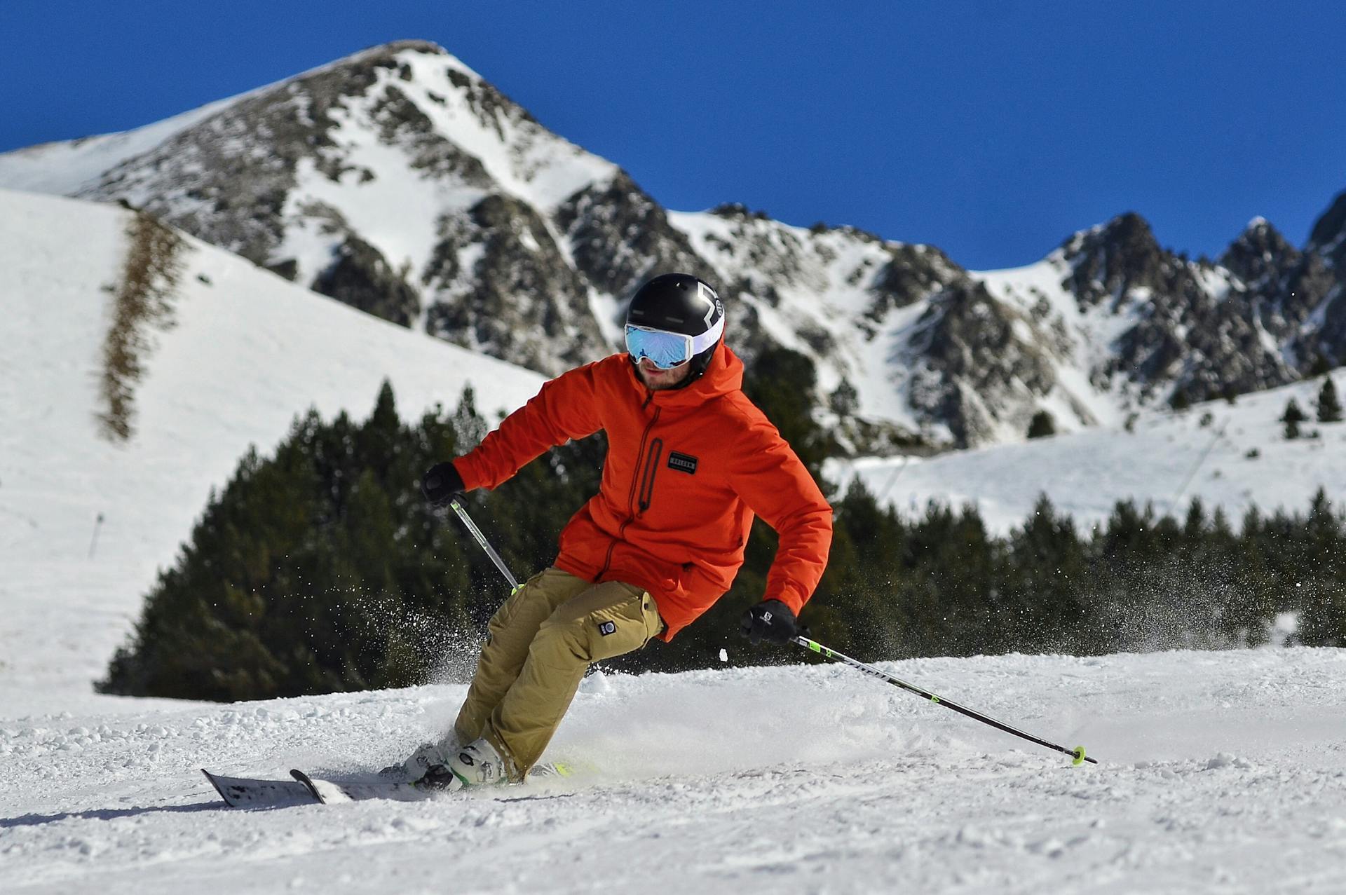 photo of a man in an orange jacket and beige trousers skiing