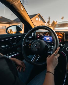 Interior view of luxury car steering and dashboard while driving at sunset.