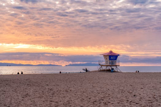 Peaceful Huntington Beach sunset with lifeguard tower silhouette and serene ocean backdrop.