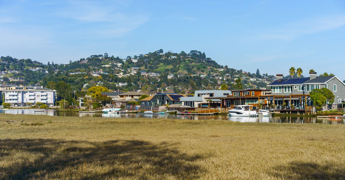 Peaceful waterfront community with modern homes and boats against a lush, green hillside backdrop.