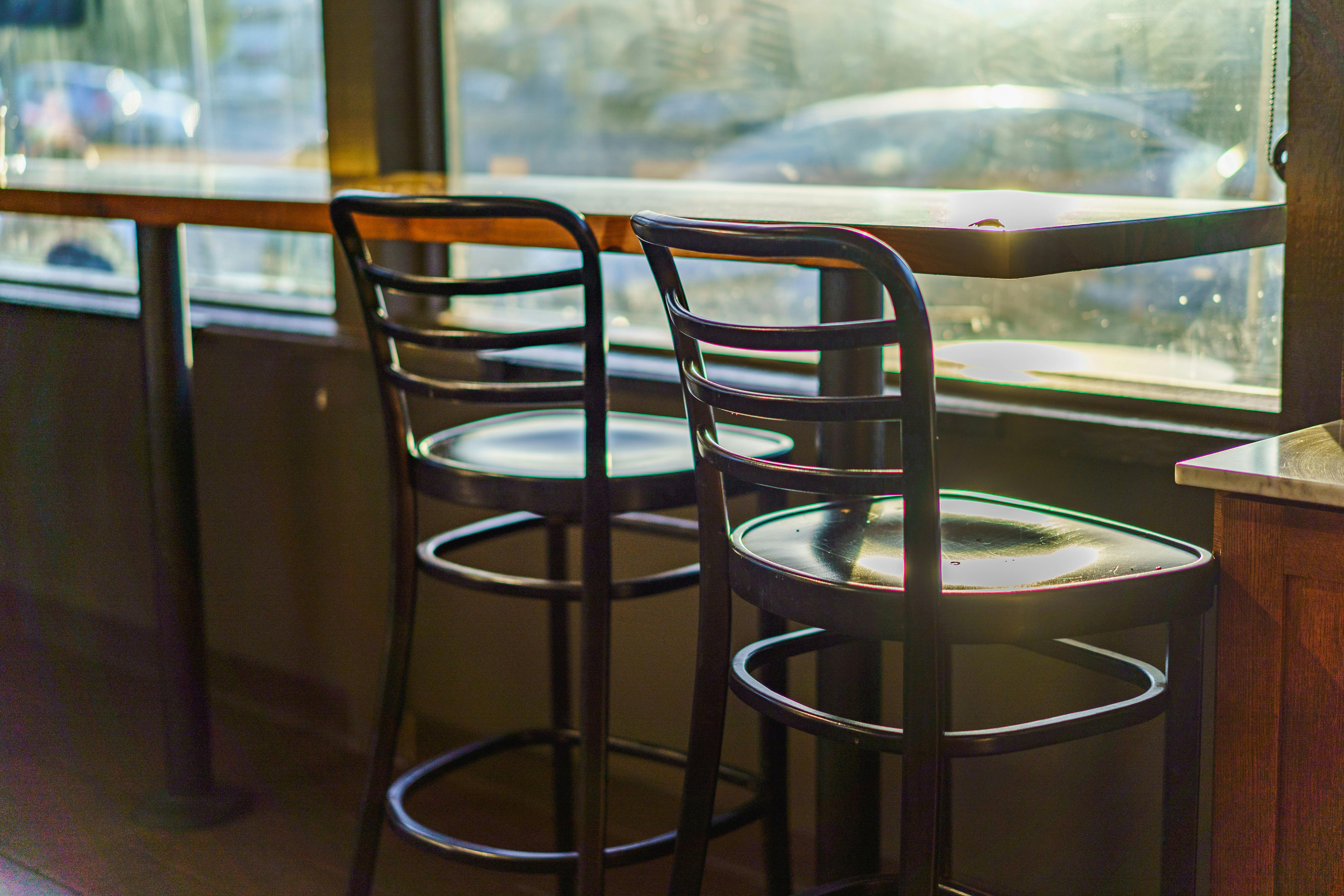 Kostnadsfria Två tomma caféstolar vid ett solbelyst fönster, vilket skapar en varm och inbjudande atmosfär. Stock foto