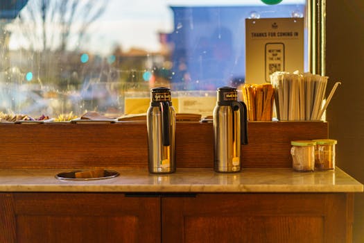 Stainless steel coffee dispensers and stirrers at a cozy cafe station with warm lighting.