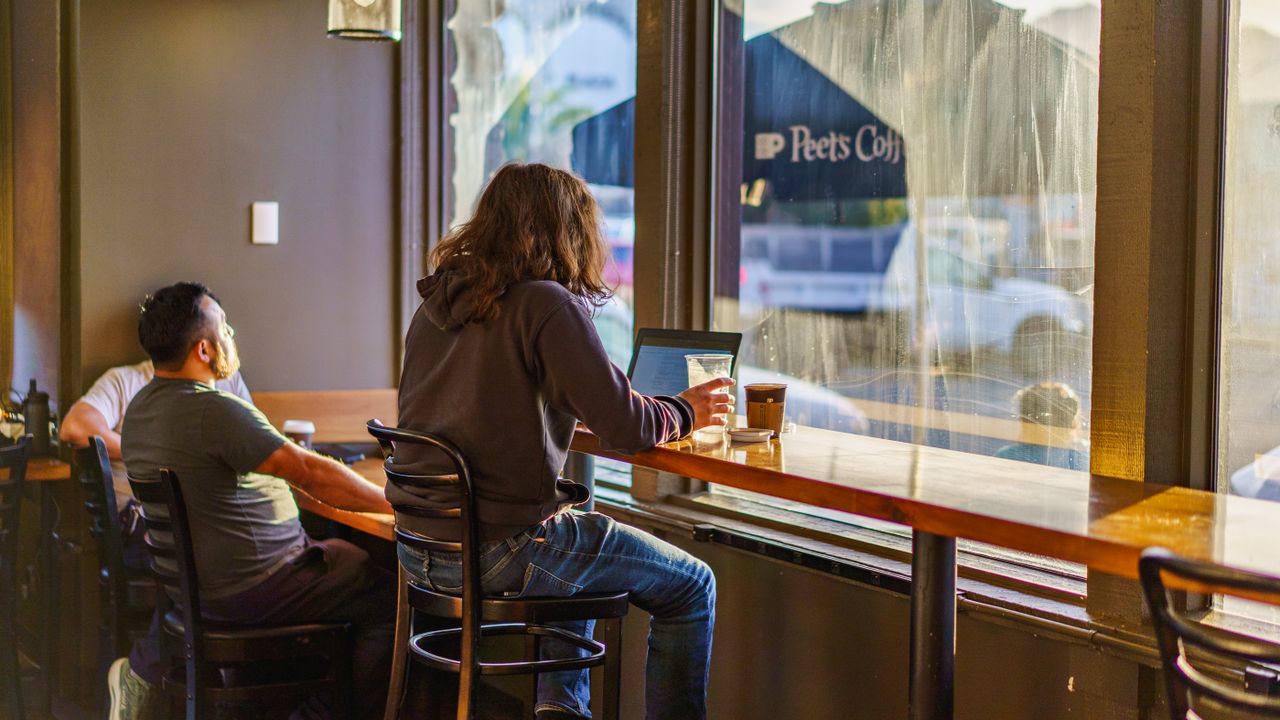 Two young adults enjoy a quiet moment in a coffee shop with warm natural lighting.