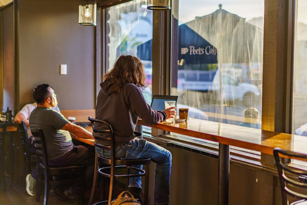 Two young adults enjoy a quiet moment in a coffee shop with warm natural lighting.